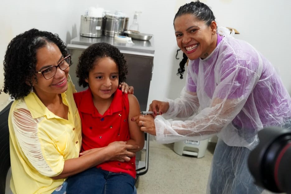 Goiânia e Aparecida antecipam ampliação da vacinação contra gripe - criança no colo da mãe recebendo vacina